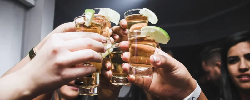 Alcoholgebruik kanker; proostende mensen met shotjes tequilla in de hand.